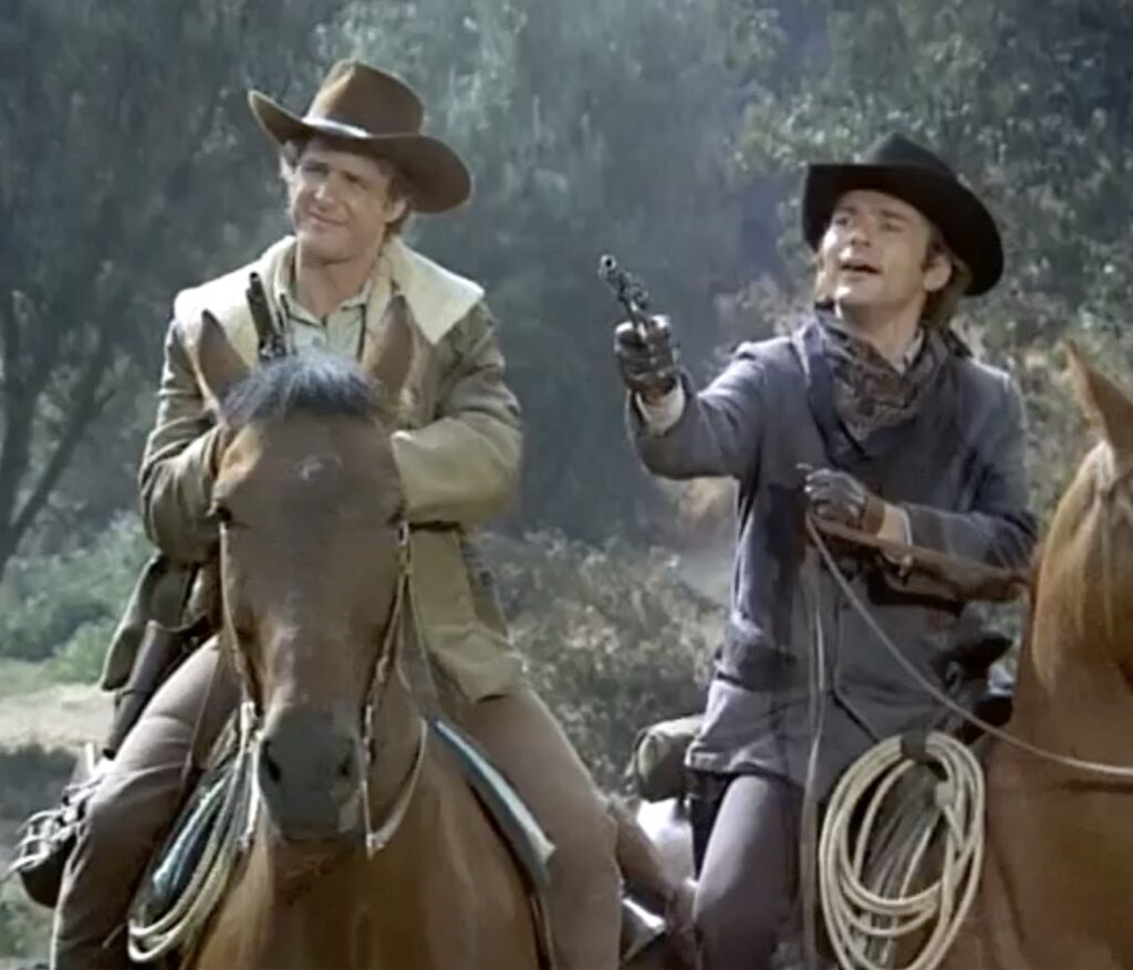 Two men in cowboy hats on horses; one gesturing with a revolver.