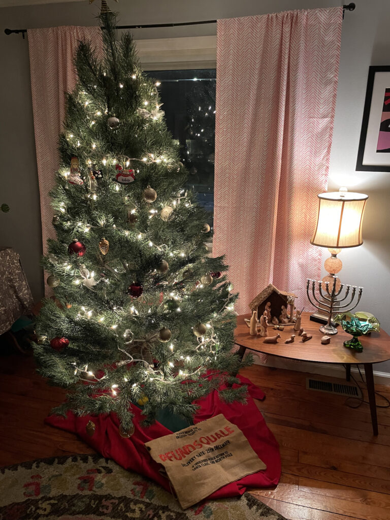 a Christmas tree with ornaments; next to it, a table with a Nativity scence, menorah, and dreidel