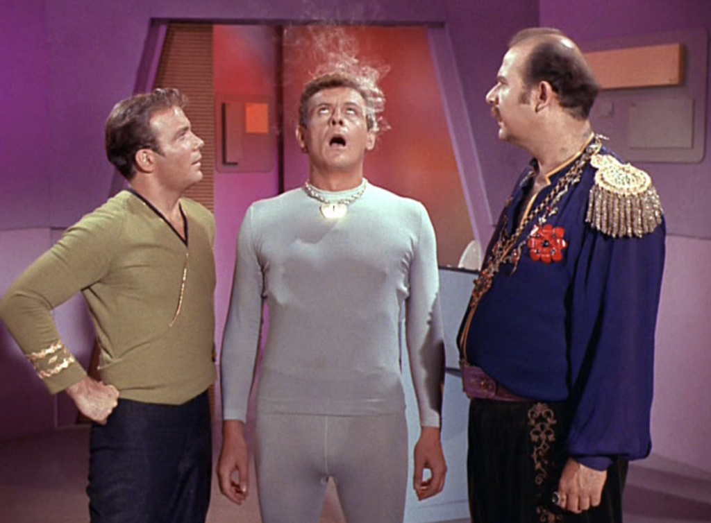 The screenshot from the penultimate scene of the episode shows the chief android Norman (Richard Tatro) with smoke coming out of his head, flanked by Captain Kirk (William Shatner) and Harry Mudd (Roger C Carmel). 
